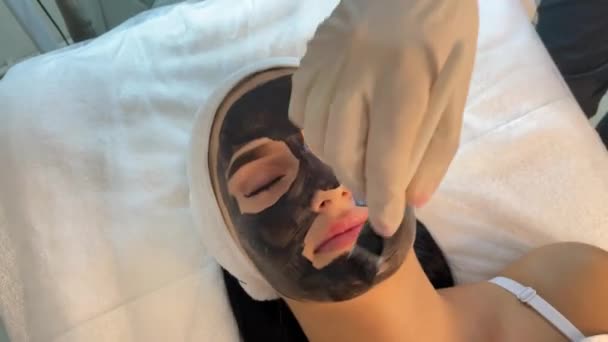 Cosmetoloog Toepassen Van Zwart Masker Mooie Vrouw Gezicht Dragen Van — Stockvideo