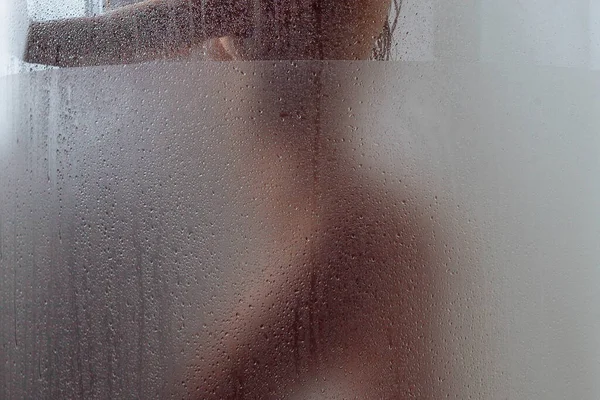 一个裸体少女洗淋浴 她模糊的身影是可见通过汗水玻璃表面有水滴和溪流 重点是湿的玻璃墙上的淋浴房 — 图库照片
