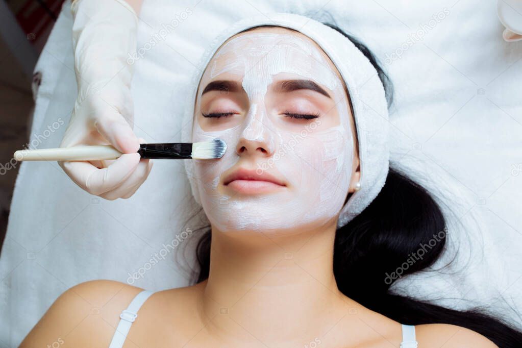 Facial cosmetic procedure in spa salon. The procedure for applying a mask to the face of a beautiful woman.