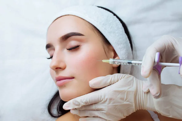 Smile lifting and lip augmentation. Beautician doctor hands doing beauty procedure to female face with syringe. Young woman\'s mouth contouring with filler injection. Marionette lines treatment.