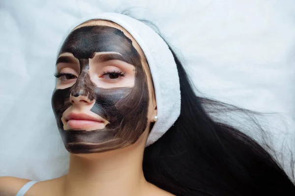 Косметолог надевает черную маску на красивую женщину в черных перчатках, великолепная женщина в спа проходит процедуры по уходу за лицом — стоковое фото
