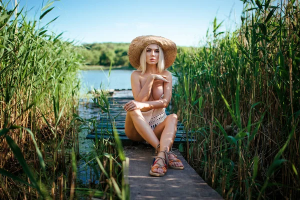 Mooi model meisje poseren op het veld genieten van de natuur buiten in een strohoed. schoonheid blond jong vrouw met lange rechte blond haar close up portret — Stockfoto