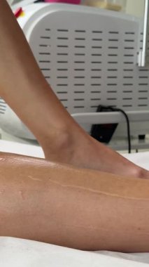 Güzellik salonu. Pembe eldiven giyen bir kozmetolog, saç çıkarma işlemi sırasında bir kadının bacağına jöle sürer. Saç çıkarma işlemi tam gaz devam ediyor.