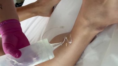 Güzellik salonu. Pembe eldiven giyen bir kozmetolog, saç çıkarma işlemi sırasında bir kadının bacağına jöle sürer. Saç çıkarma işlemi tam gaz devam ediyor.