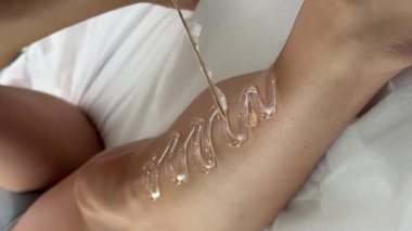 Güzellik salonu. Pembe eldiven giyen bir kozmetolog, saç çıkarma işlemi sırasında bir kadının bacağına jöle sürer. Saç çıkarma işlemi tam gaz devam ediyor.