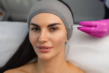 Genç kozmetolojistin kadın yüzüne botoks enjekte eden ellerini yakın. Ayakta duruyor ve gülümsüyor. Kadın rahatlama ile gözlerini kapattı.