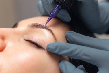 Kadın bir müşteriye kaş mikroplu pateni yapan bir kozmetikçiye yakın çekim. Profesyonel güzellik prosedürü, steril aletler, hassas işler ve modern bir güzellik stüdyosunda kaş şekillendirme.