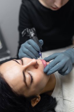 Kalıcı dudak makyajı yapan bir kozmetolojiste yakın çekim, profesyonel bir güzellik stüdyosunda doğal dudak rengini steril aletlerle dövme yaptırmak.