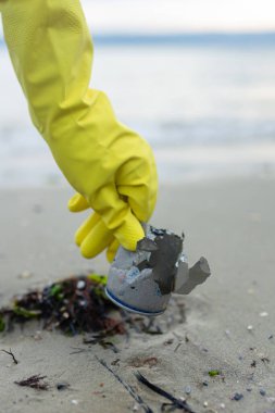Plaj temizliği, kirlilik, atık sorunu, ekoloji, sahil koruma ve çevre bilincinin altını çizerek ezilmiş metal bir teneke kutu almaya gönüllü olan gönüllüler