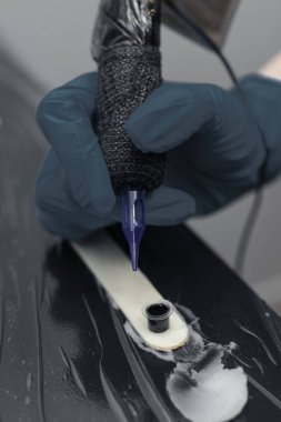 Dövme sanatçısı dövme makinesini hazırlıyor, dövme işlemine başlamadan önce iğneyi siyah mürekkebe batırıyor.