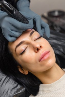 Kadın bir müşteriye kaş mikroplu pateni yapan bir kozmetikçiye yakın çekim. Profesyonel güzellik prosedürü, steril aletler, hassas işler ve modern bir güzellik stüdyosunda kaş şekillendirme.