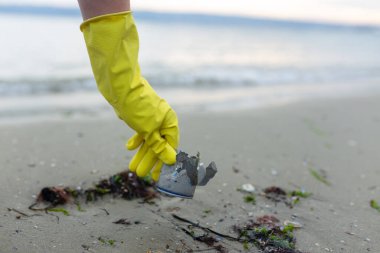 Plaj temizliği, kirlilik, atık sorunu, ekoloji, sahil koruma ve çevre bilincinin altını çizerek ezilmiş metal bir teneke kutu almaya gönüllü olan gönüllüler