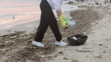 Kirli bir plajda plastik çöpleri temizlemeye gönüllü olan bir gönüllü. Şişeleri toplayıp çöp torbasına atıyorlar. Çevre koruma, ekoloji farkındalığı, sahil temizliği ve okyanus kirliliği sorunu