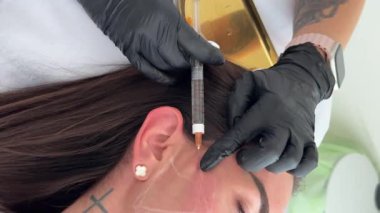 Estetik tıp: Siyah eldivenli kozmetik uzmanı tarafından kadınlara kanül enjeksiyonuyla kolajen biyo-evrizasyon tedavisine yakın çekim.