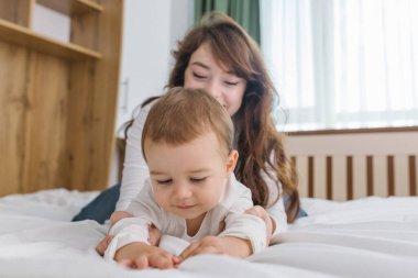 Genç anne evde bebeğiyle oynuyor. Şefkat, rahatlık, doğal ışık ve neşeli ebeveyn-çocuk bağıyla dolu sıcak ve rahat bir aile anının tadını çıkarıyor.