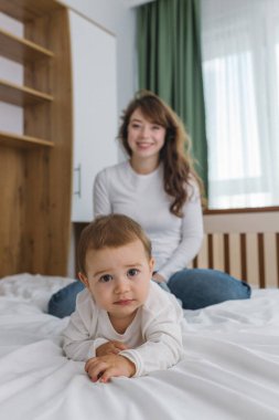 Genç anne evde bebeğiyle oynuyor. Şefkat, rahatlık, doğal ışık ve neşeli ebeveyn-çocuk bağıyla dolu sıcak ve rahat bir aile anının tadını çıkarıyor.