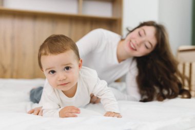 Genç anne evde bebeğiyle oynuyor. Şefkat, rahatlık, doğal ışık ve neşeli ebeveyn-çocuk bağıyla dolu sıcak ve rahat bir aile anının tadını çıkarıyor.