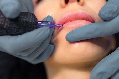 Kalıcı dudak makyajı yapan bir kozmetolojiste yakın çekim, profesyonel bir güzellik stüdyosunda doğal dudak rengini steril aletlerle dövme yaptırmak.