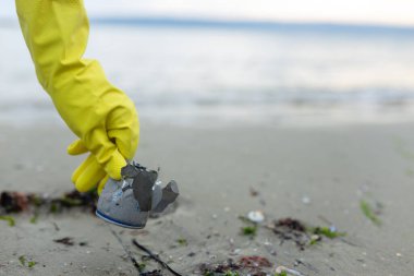 Plaj temizliği, kirlilik, atık sorunu, ekoloji, sahil koruma ve çevre bilincinin altını çizerek ezilmiş metal bir teneke kutu almaya gönüllü olan gönüllüler