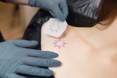 Dövme sanatçısı bir müşteri göğsüne güneş tasarımı kalıbı uyguluyor, dövme oturumuna başlamadan önce yerleştirmeyi hazırlıyor