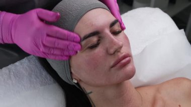 Yüz masajı seansı. Pembe eldivenli estetik uzmanı estetik tedaviden sonra bir kadının yüzüne nazikçe masaj yapıyor. Yakın çekim, profesyonel cilt bakımı prosedürü