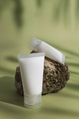 Doğal taşın üzerine yumuşak yeşil arka planlı kozmetik krem tüpleri, temiz cilt bakımı güzellik, sağlık, organik ürünler ve minimalist markalaşma için modelleme.