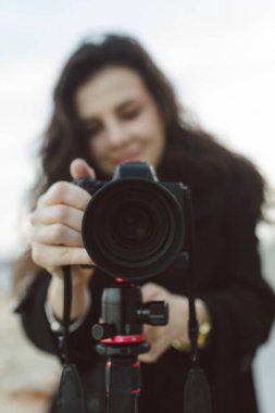 Kadın fotoğrafçı, deniz kenarındaki tripoda profesyonel kamerayı ayarlıyor. Kayalık bir sahil şeridinde yaratıcı bir fotoğraf çekimine hazırlanırken objektife odaklanıyor.