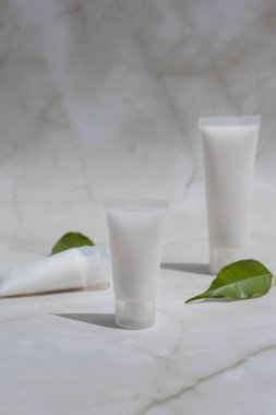 Mermer yüzeyinde boş kozmetik tüpleri ve yeşil yapraklarla minimalist cilt modeli, doğal güzellik ürünleri, organik markalaşma, temiz kozmetik ürünleri ve modern sağlık tasarımı için idealdir.