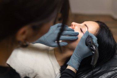 Bir kozmetik uzmanının göz kapağı makyajı, göz kalemi dövme prosedürünü steril aletlerle gerçekleştirmesi profesyonel bir stüdyoda kırbaç çizgisini ve göz güzelliğini artırması.