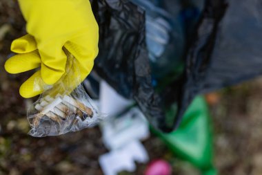 Sarı eldivenli bir gönüllü, kirli bir plajda sigara izmaritleri topluyor. Çevre temizliği, ekoloji koruması, kıyı şeridi atıkları ve çöp önleyici farkındalık