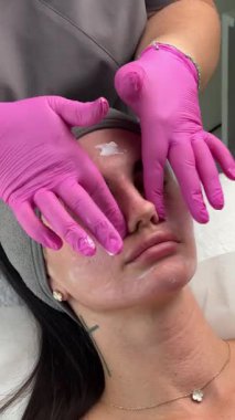 Yüz masajı seansı. Pembe eldivenli estetik uzmanı estetik tedaviden sonra bir kadının yüzüne nazikçe masaj yapıyor. Yakın çekim, profesyonel cilt bakımı prosedürü