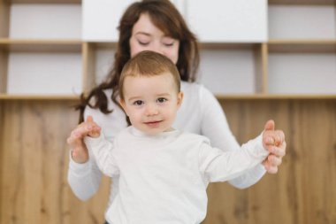 Genç anne evde bebeğiyle oynuyor. Şefkat, rahatlık, doğal ışık ve neşeli ebeveyn-çocuk bağıyla dolu sıcak ve rahat bir aile anının tadını çıkarıyor.
