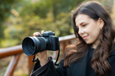 Sıcak güneş ışığında dışarıda fotoğraf çekerken elinde dijital kamerayla genç bir kadının yakın çekimi. Yumuşak altın saat ışığı, yaratıcı yaşam tarzı fotoğrafçılık anı