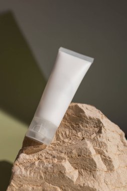 Doğal taşın üzerinde duran boş kozmetik tüpüyle minimum güzellik ürünü modeli, organik cilt bakımı, modern markalaşma ve temiz kozmetik ambalaj tasarımı için sıcak ışık ve toprak tonlarıyla şekillendirilmiş.