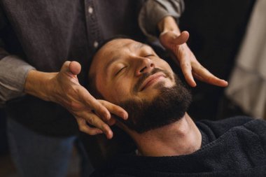 Berber dükkanında tıraş olduktan sonra sakal ve erkek müşterinin boynuna masaj yapıyor. Rahatlatıcı tımar hizmeti, erkeklerin kendi başının çaresine bakması, rahatlık ve klasik berber ritüeli kavramı.