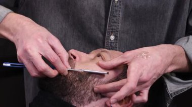 Profesyonel berberin, berber dükkanında jiletle erkek boynu traş etmesine yakın çekim. Sakal şekillendirme, klasik ıslak tıraş, erkek tımar hizmeti ve berber işi kavramı.