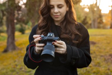 Sıcak güneş ışığında dışarıda fotoğraf çekerken elinde dijital kamerayla genç bir kadının yakın çekimi. Yumuşak altın saat ışığı, yaratıcı yaşam tarzı fotoğrafçılık anı