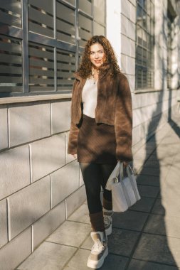 Günışığında modern binanın ön cephesinde genç bir kadın portresi. Şık günlük kıyafetler, yumuşak gölgeler, kendine güvenen görünüş, çağdaş şehir yaşam tarzı ve moda konsepti.