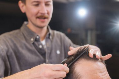 Berber, erkek müşteri saçını makas ve tarak ile kesiyor. Profesyonel saç kesim süreci, hassasiyet tekniği, modern berber dükkanında erkek bakımı.