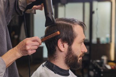 Modern berber dükkanında saç kurutma makinesi ve fırça kullanan profesyonel berber. Erkekler bakım hizmeti, saç kesimi, sakal bakımı ve yaşam tarzı konsepti