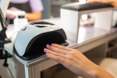 Güzellik salonundaki UV LED lambanın altındaki kadın el jölesi ojesini kapat. Profesyonel manikür süreci, tırnak kurutma, kozmetik tedavi, hijyen ve tırnak bakımı konsepti