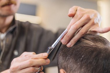 Berber, erkek müşteri saçını makas ve tarak ile kesiyor. Profesyonel saç kesim süreci, hassasiyet tekniği, modern berber dükkanında erkek bakımı.