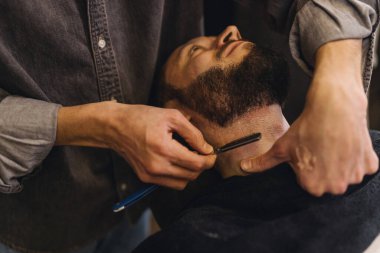 Profesyonel berberin, berber dükkanında jiletle erkek boynu traş etmesine yakın çekim. Sakal şekillendirme, klasik ıslak tıraş, erkek tımar hizmeti ve berber işi kavramı.