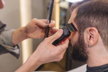 Berber berber dükkanında elektrikli makasla erkek müşterinin sakalını kesiyor. Profesyonel tımar süreci, sakal şekli, erkeklerin saç bakım rutini, klasik berber servisi.