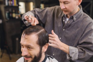 Berber, erkek müşteri saçını makas ve tarak ile kesiyor. Profesyonel saç kesim süreci, hassasiyet tekniği, modern berber dükkanında erkek bakımı.