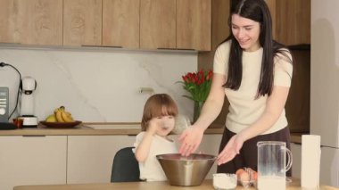 Anne ve küçük kızı modern mutfakta birlikte yemek pişiriyor, mutlu aile yemekleri yapıyor ve birlikte vakit geçiriyorlar.