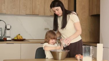 Anne ve küçük kızı modern mutfakta birlikte yemek pişiriyor, mutlu aile yemekleri yapıyor ve birlikte vakit geçiriyorlar.