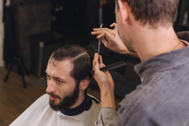 Berber, erkek müşteri saçını makas ve tarak ile kesiyor. Profesyonel saç kesim süreci, hassasiyet tekniği, modern berber dükkanında erkek bakımı.