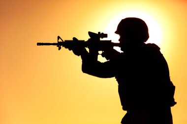 Asker gün batımında tüfekle ateş ediyor.