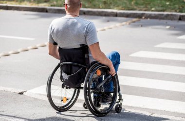 Tekerlekli sandalyedeki engelli adam yaya geçidinden karşıya geçmeye hazırlanıyor.
